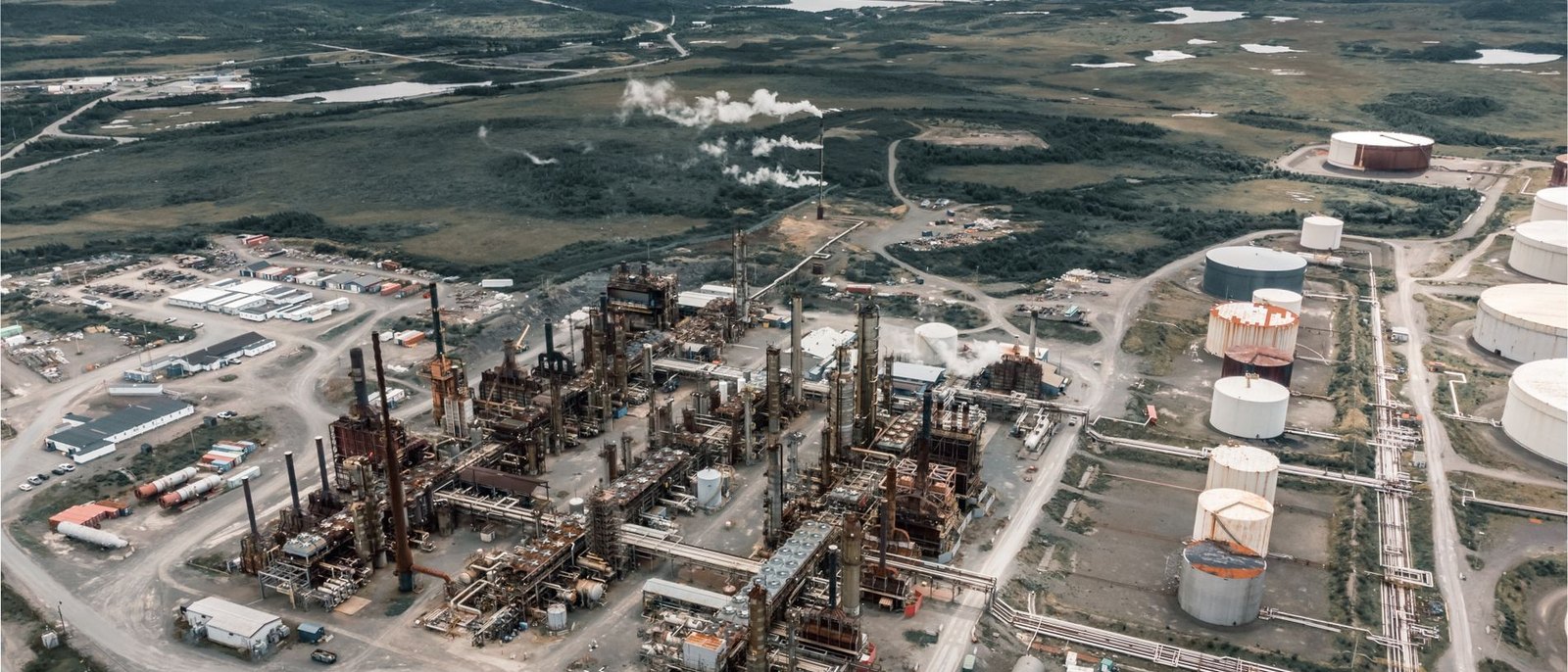 Aerial view of an oil and gas processing facility showing tank batteries, pipe racks, processing units, and a service yard with equipment and buildings